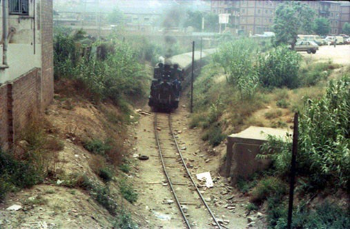 Tren de vapor circulando por una vía junto a Montjuïc